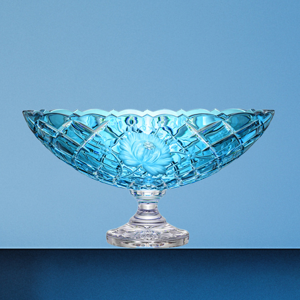 Oval jardinières in azure blue lead crystal with an elegant diamond pattern. In the centre is a detailed sun rose engraving. Hand-cut crystal glass shimmers in turquoise on a clear base against a blue background.