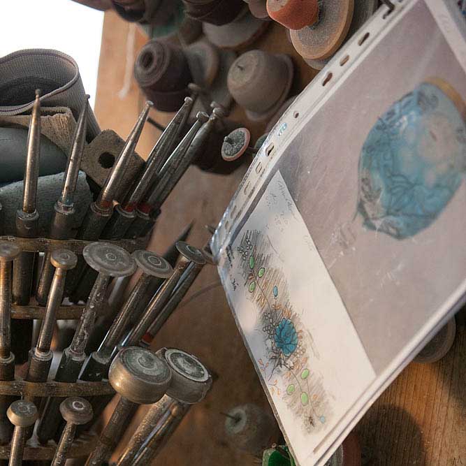Tools for deep-cutting crystal glasses and decorative designs in a workshop. Tapered and round metal cutting tools in holders, alongside floral sketches and a design for a blue Ginglas.