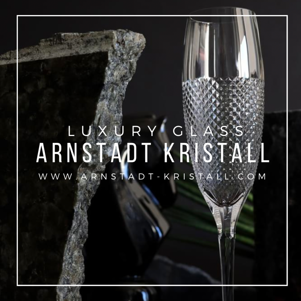 An elegant, clear champagne glass from ARNSTADT KRISTALL, hand-blown and hand-cut. Oxford bowl with a precise, faceted diamond cut at the base; stem and upper bowl smooth. Against a dark, stone-like background.