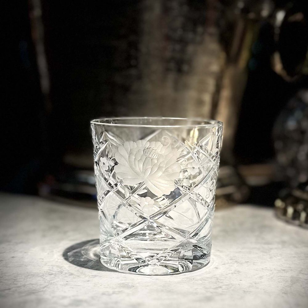 ARNSTADT KRISTALL Sunrose whisky glass, artfully cut with a diamond pattern and a large, elegant flower. Set against a dark background, the light-coloured surface and thick base cast a clear shadow.