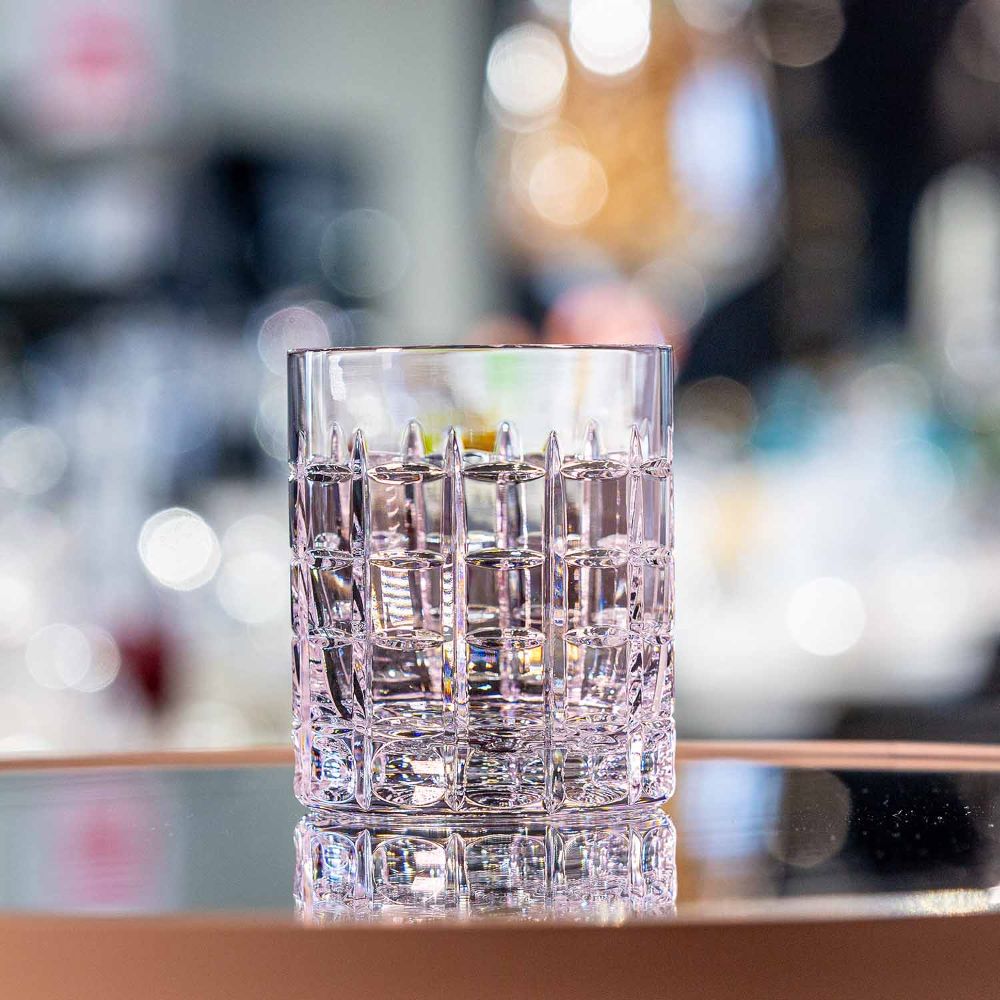 Empty crystal whisky glass in a Las Vegas design with an intricate square cut pattern that elegantly reflects the light. On a reflective surface that emphasises the thick glass base. Blurred background with bright bokeh lights.