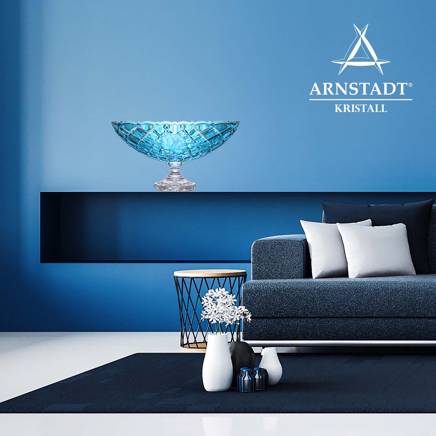 Azure blue crystal jardinières from the Sunrose collection on a dark shelf against a light blue wall. Intricate cutwork with floral motifs and a clear, light-reflecting base. Below: blue sofa, side table with flowers.